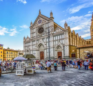 Belebter Platz vor der Basilika Santa Croce in Florenz, Italien, mit zahlreichen Touristen, Fahrr&auml;dern und einem Souvenirstand bei strahlend blauem Himmel.