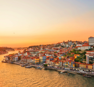 Abendstimmung &uuml;ber der Altstadt von Porto, Portugal, mit bunten H&auml;usern am Flussufer und goldener Himmelsf&auml;rbung.