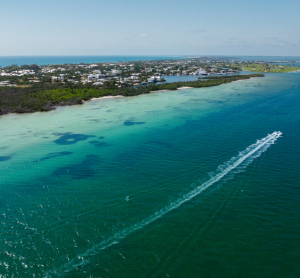 Luftaufnahme der K&uuml;ste von Florida mit t&uuml;rkisfarbenem Wasser, einem Motorboot mit wei&szlig;er Spur und H&auml;usern entlang des Strandes.