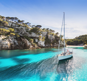Segelboot in einer türkisfarbenen Bucht zwischen bewaldeten Felsklippen.