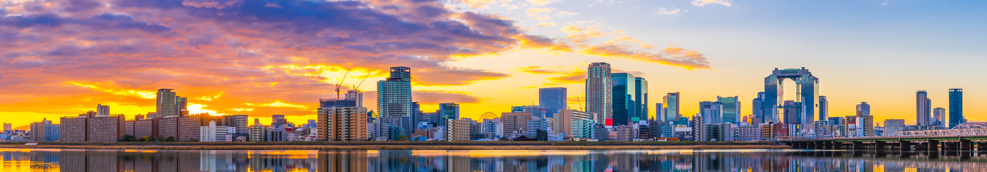 Panorama der Skyline von Osaka mit Umeda Sky Building und Fluss Yodo im Vordergrund bei Sonnenuntergang.