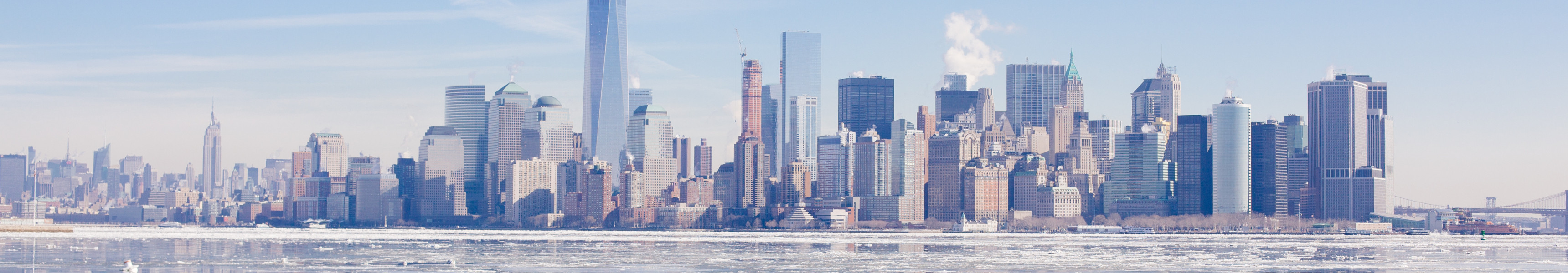 Panorama der Skyline von New York City im Winter mit dem One World Trade Center im Mittelpunkt, das sich im teilweise vereisten Hudson River spiegelt.