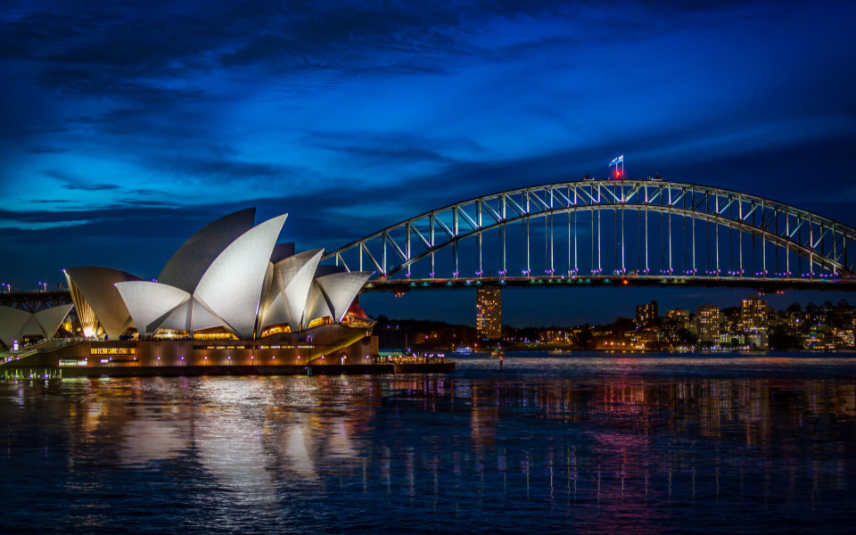 Sydney-Oper und Harbour Bridge bei Nacht mit Spiegelung im Wasser.