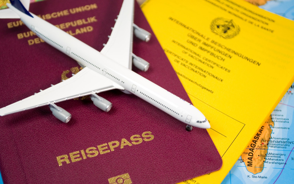 Deutscher Reisepass, gelbes Impfbuch und Modellflugzeug liegen auf einer Weltkarte.